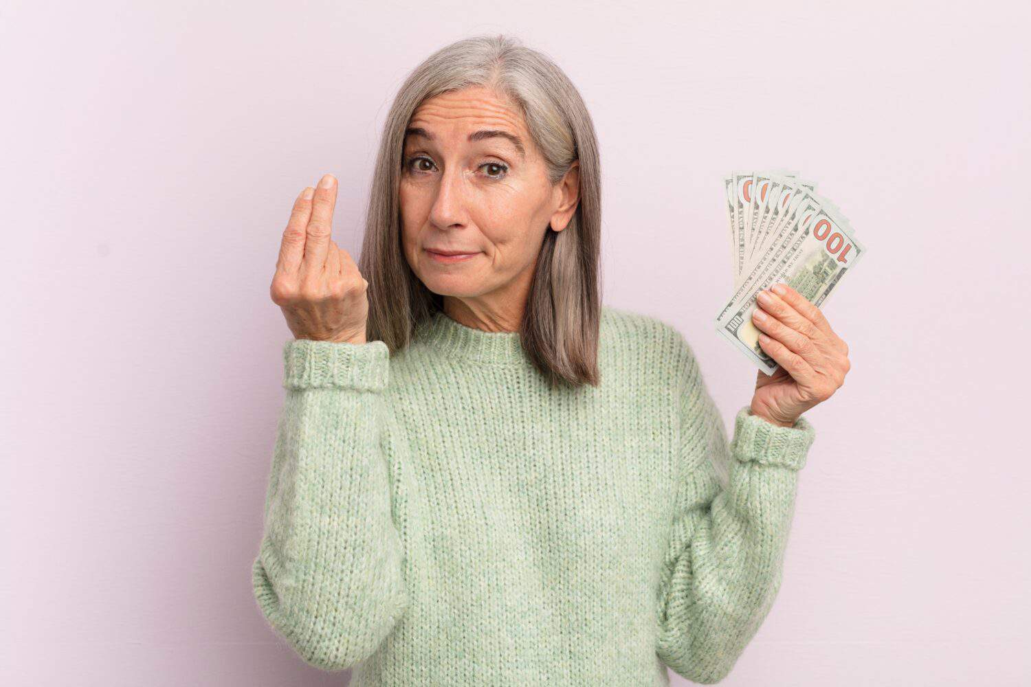 middle age woman making capice or money gesture, telling you to pay. dollar banknotes concept