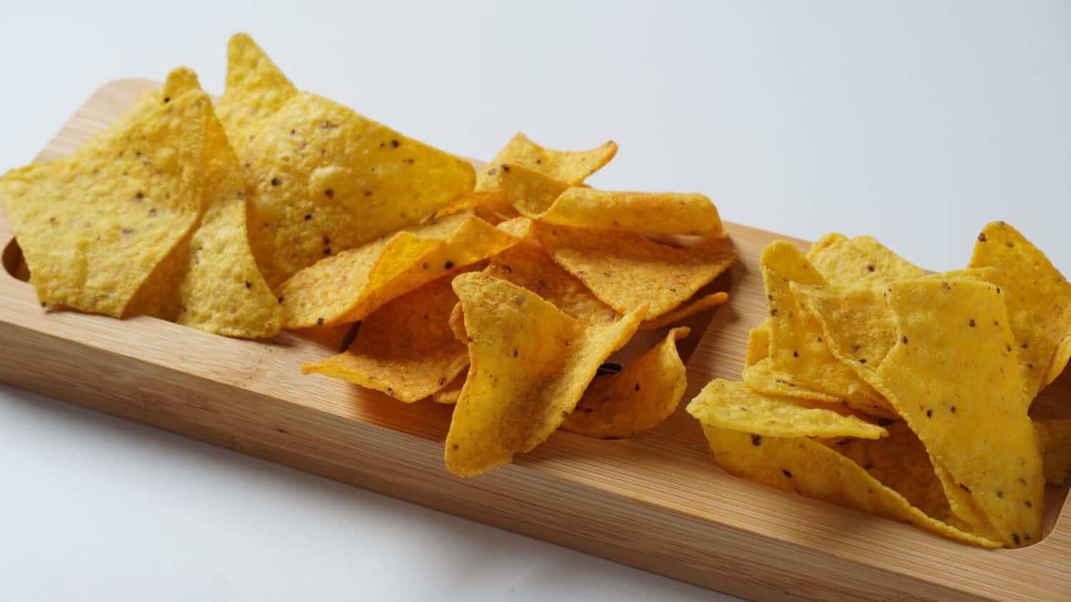 Doritos is an American brand of flavored tortilla chips. Corn chips doritos spiced on a a wooden board.