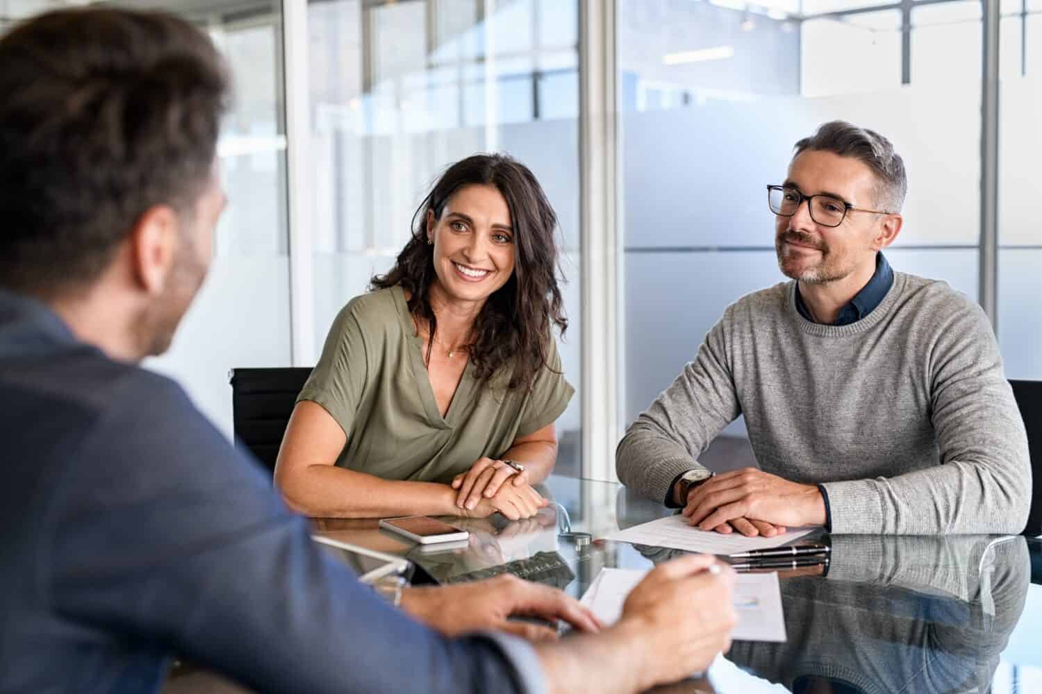 Smiling mature couple meeting with bank manager for investment. Mid adult woman with husband listening to businessman during meeting in conference room. Middle aged couple meeting loan advisor.