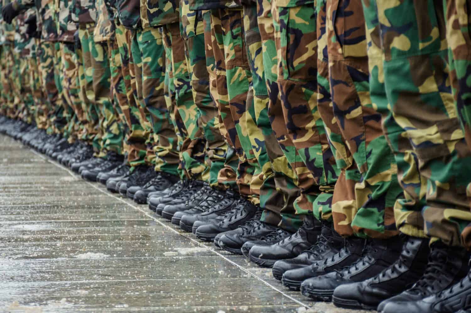 Military boots and camouflage trousers of many soldiers in uniform in a row under the rain and snow