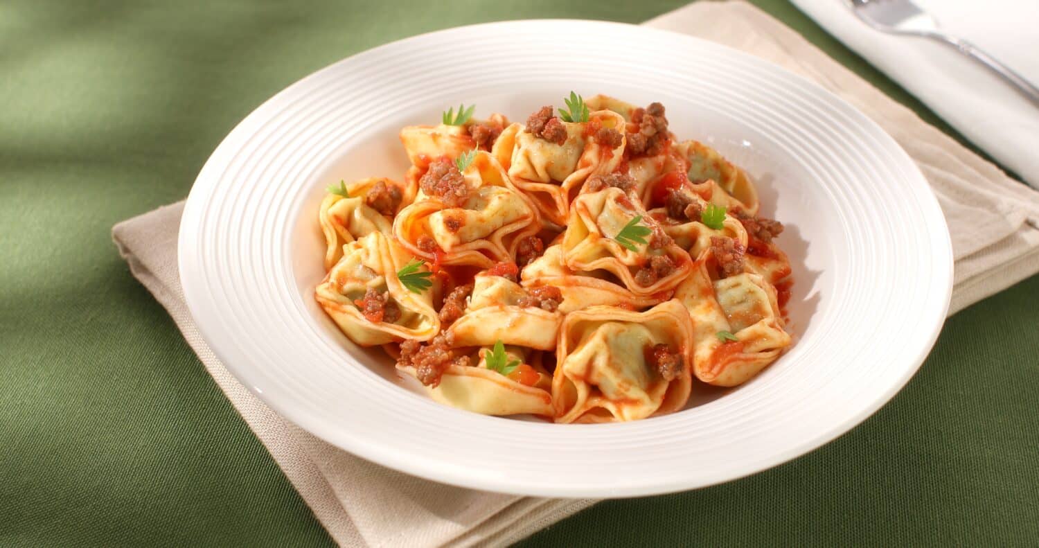 tortelloni with bolognese sauce. classic Italian pasta with spinach and ricotta in tomato-meat sauce. dish of mediterranean cuisine on a green background. food on the table on a sunny day.