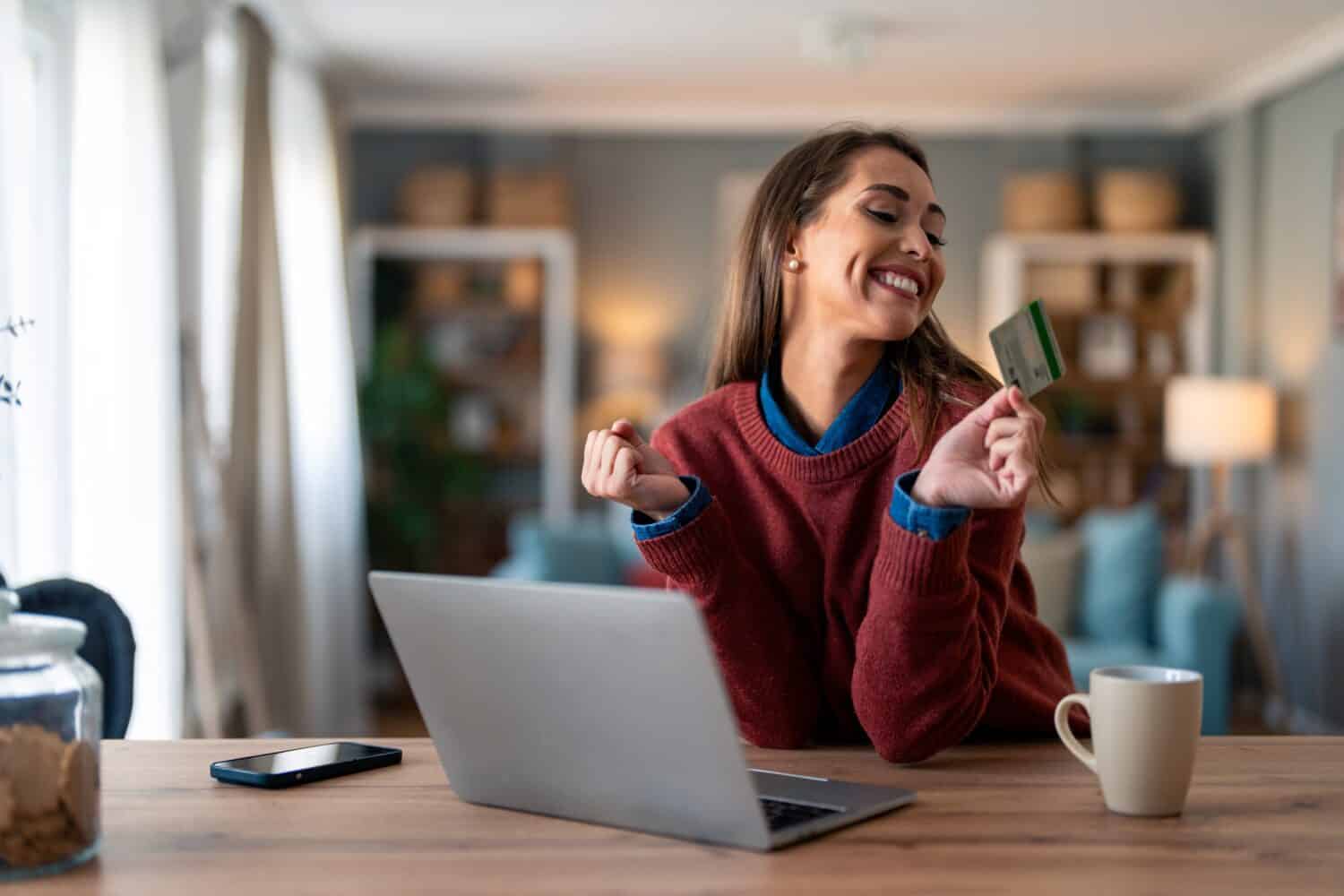 Cheerful female customer looking at credit card and pumping fist after receiving reward for online shopping.