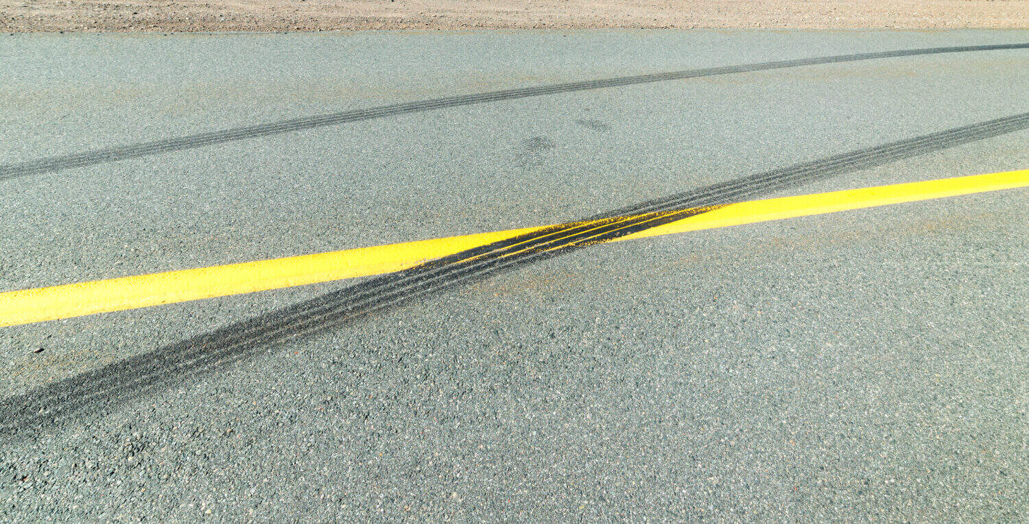 Black skid marks on a highway. The marks cross the center line. Closeup view.