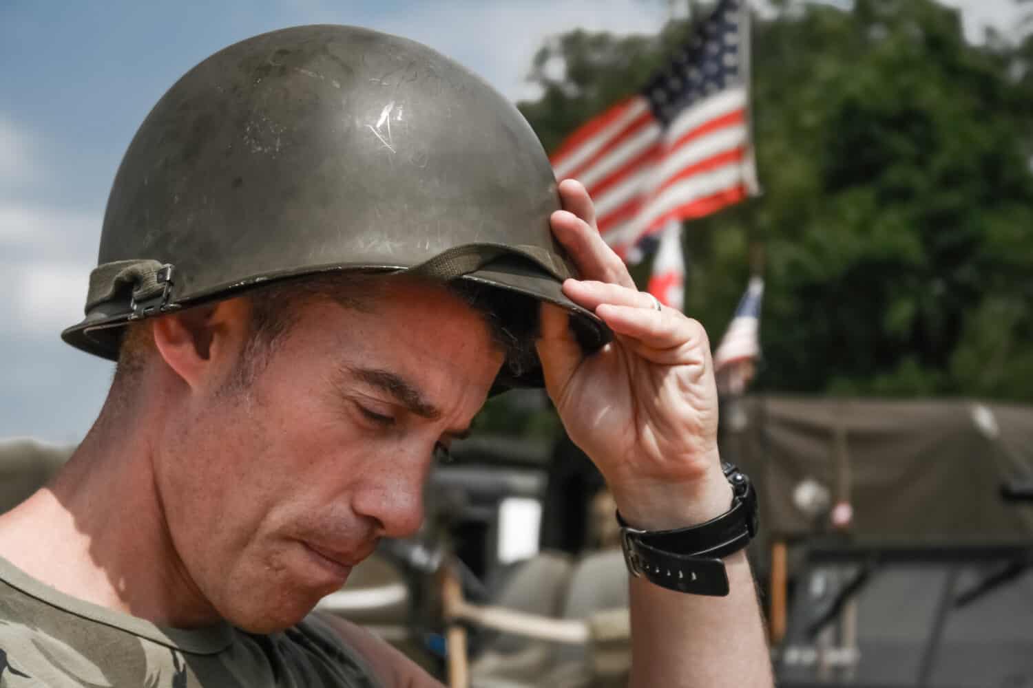 Tired Vietnam War era soldier puts oh his helmet, with American flag in background