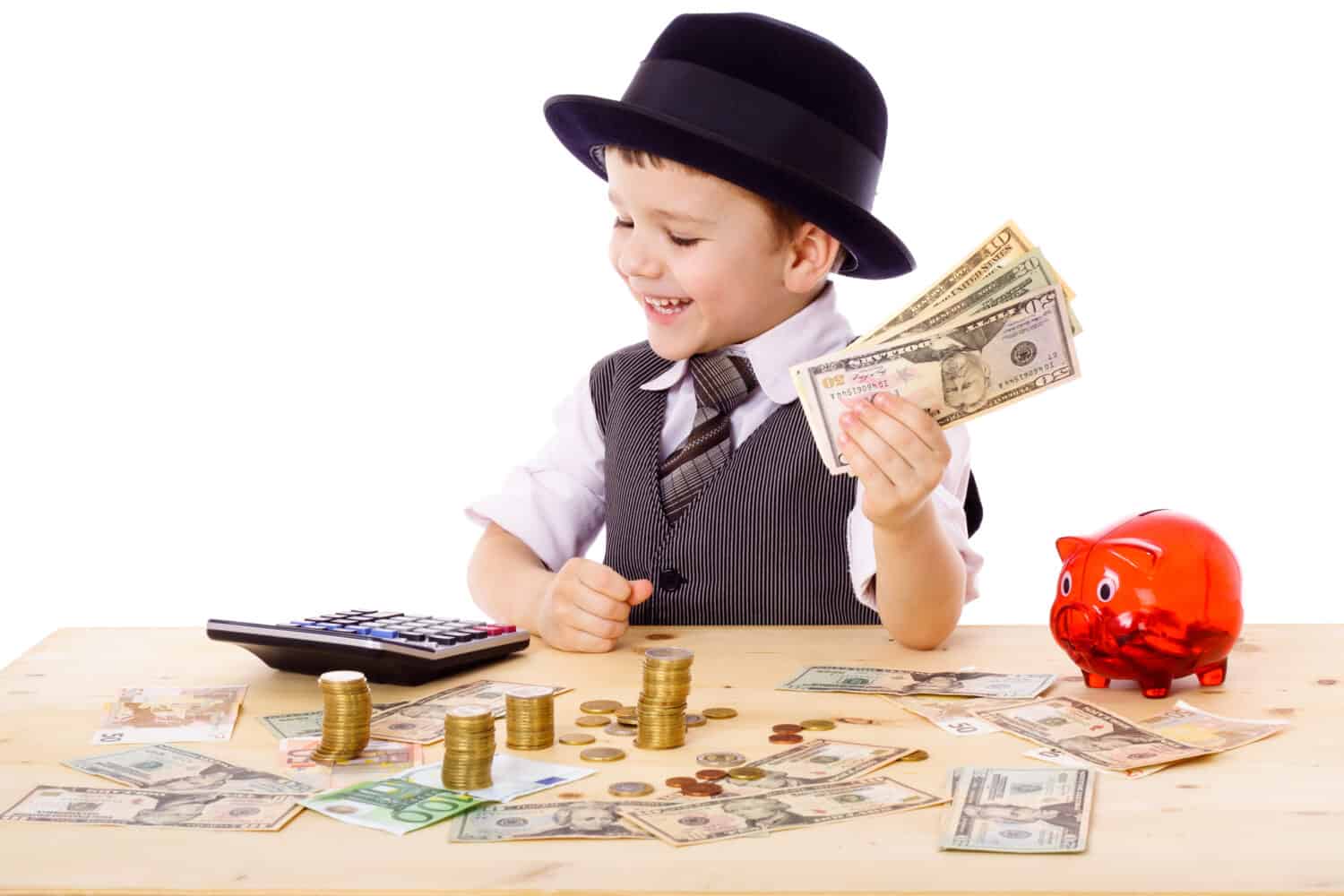 Little boy in black hat and tie at the table counts money, isolated on white