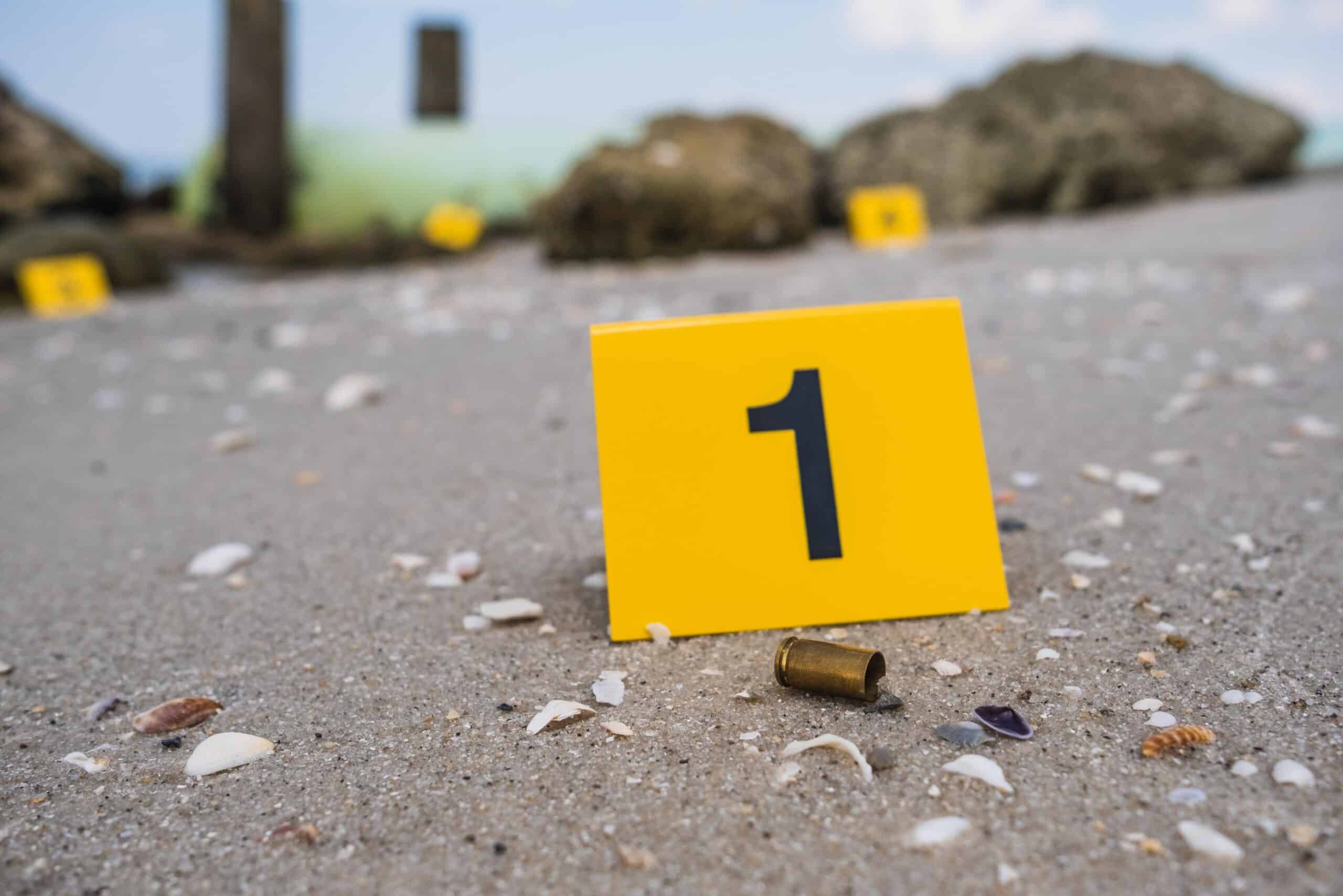 Florida gun | One yellow crime scene evidence marker on the beach after a gun shooting brass bullet shell casing 9mm handgun pistol