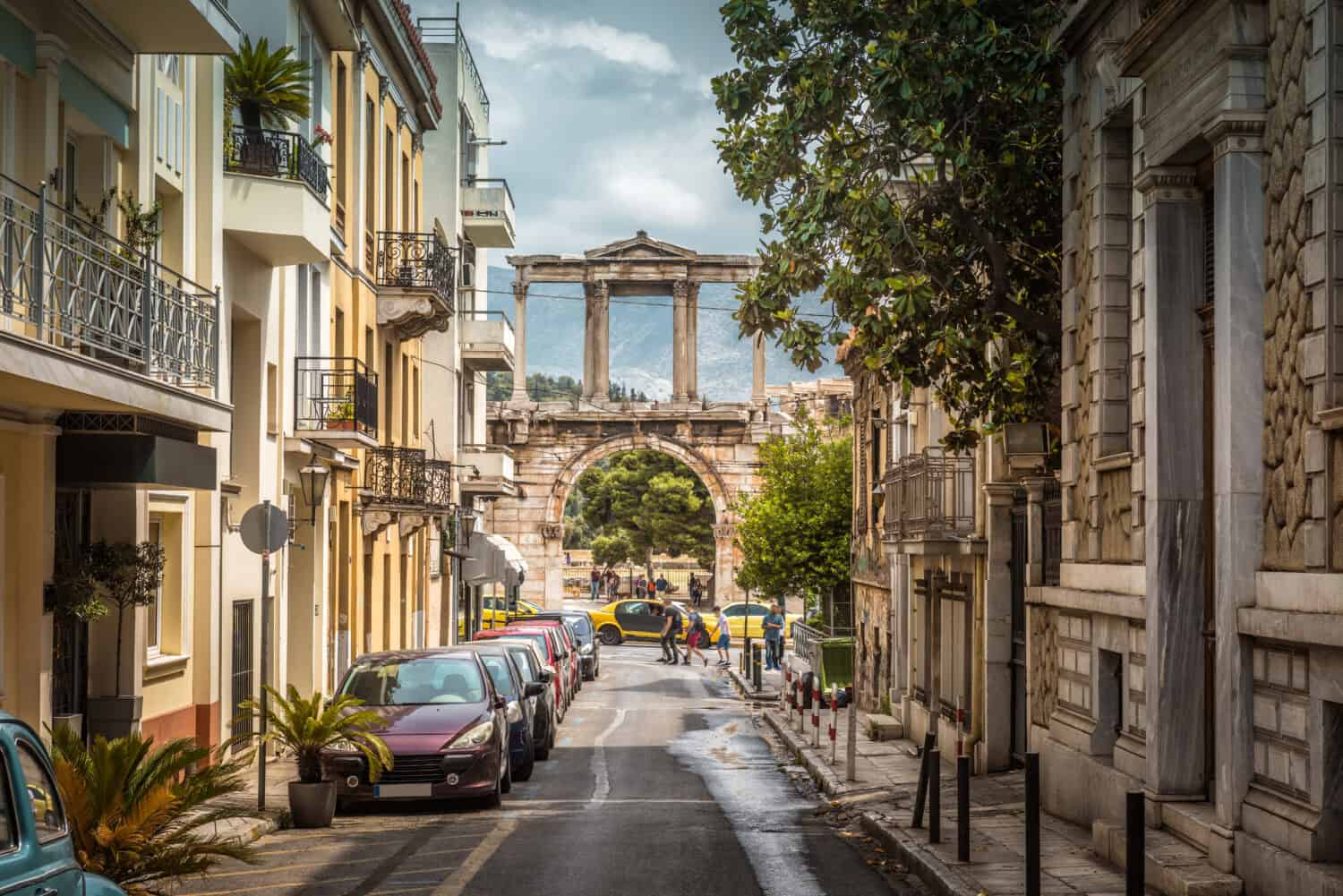 Street in Athens overlooking ancient Arch or Gate of Hadrian, Greece. It is one of main landmarks in Athens. Nice view of cozy houses, parked cars and historical monument in Athens city center.