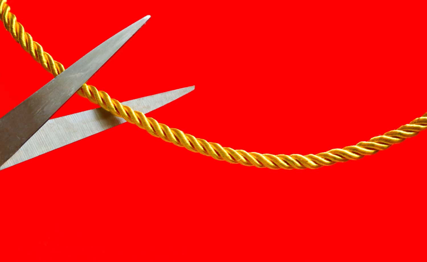 a scissors cutting a rope which tied between two sides with red background, cut relationship concept