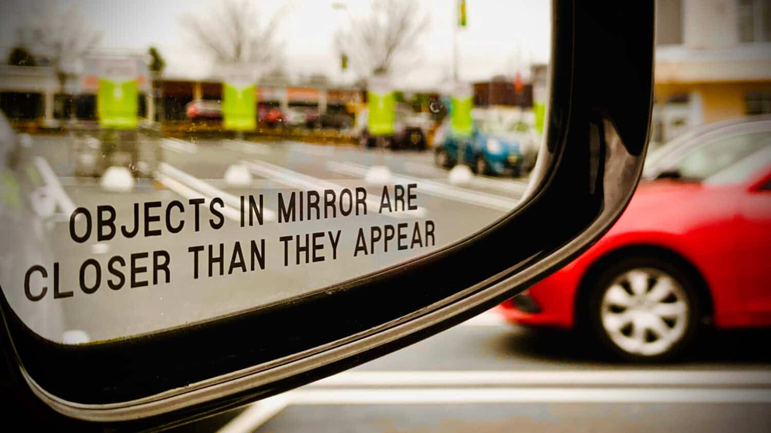 Car mirror saying “Objects In Mirror Are Closer Than They Appear” in Supermarket Parking Lot
