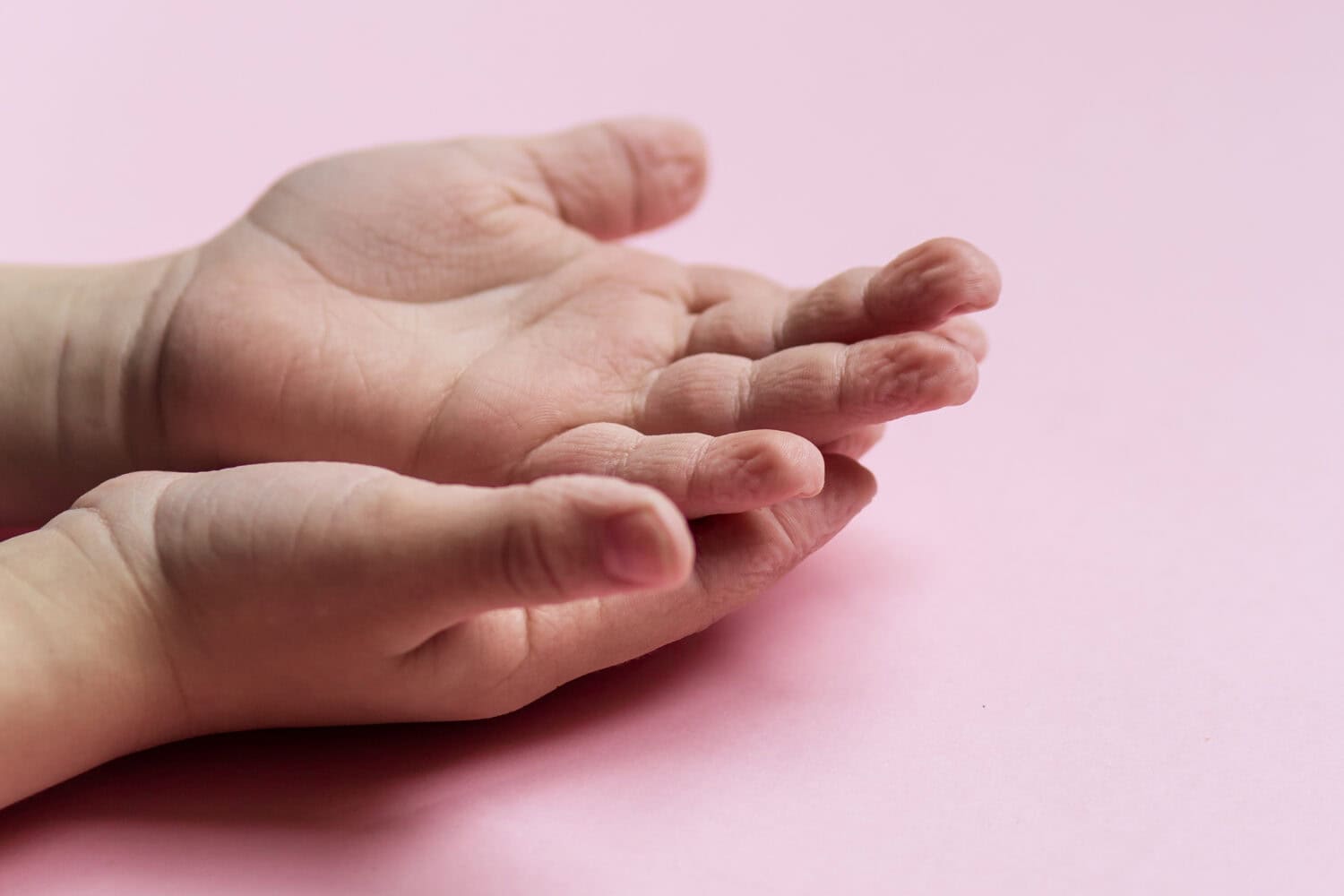 wrinkled skin on the fingers after water. Bathing in the bathroom. Long wet. Baby fingers on hand. pink background