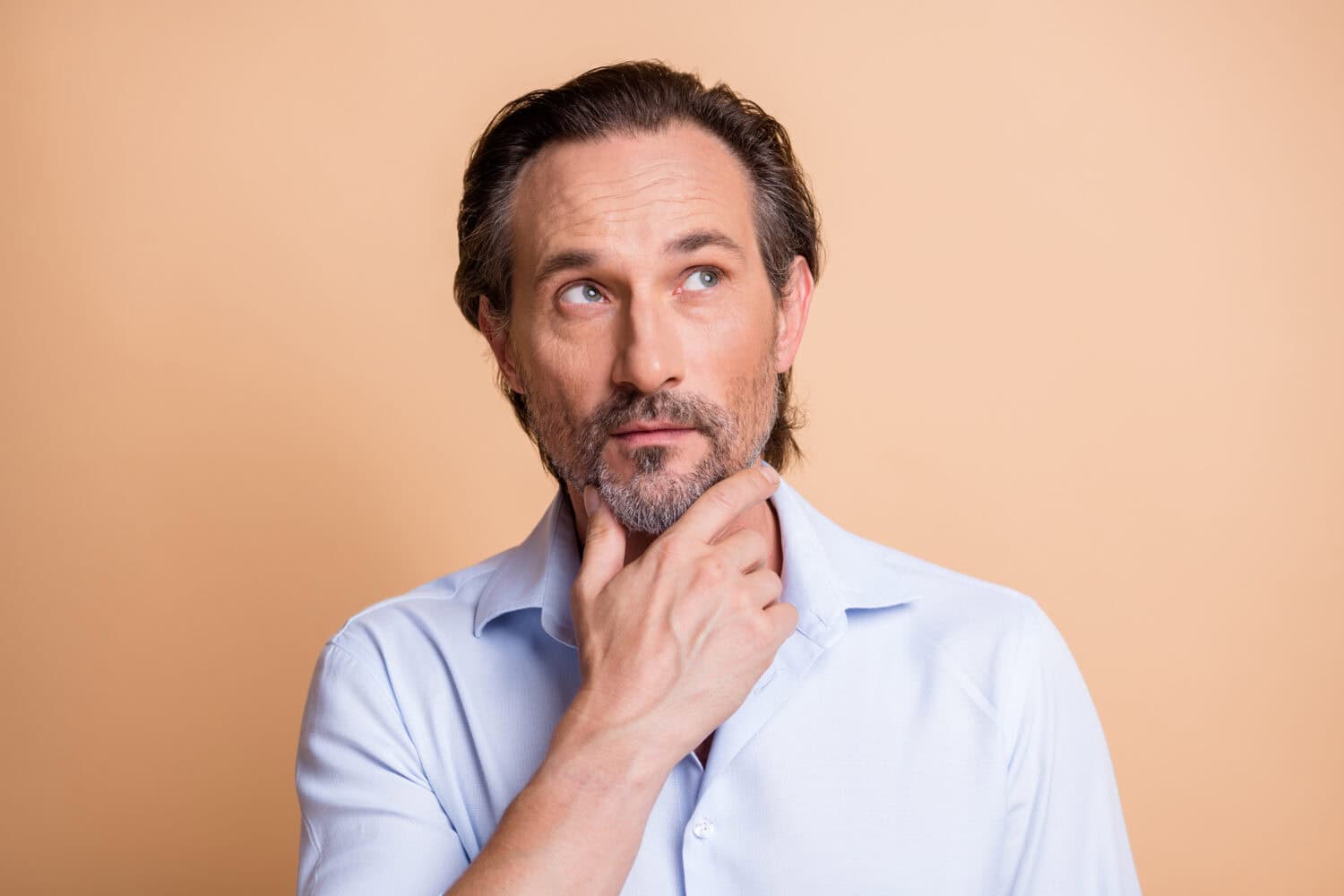 Close-up portrait of minded smart middle aged man overthinking strategy touching chin isolated over beige pastel color background