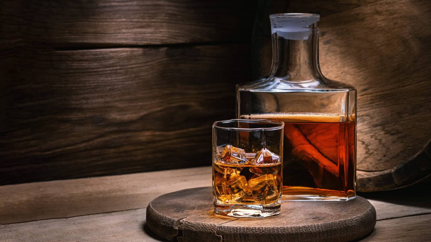 Whiskey drinks. You need to drink whiskey with ice then the whiskey tastes better of an oak barrel. Alcoholic drink with ice whiskey or cognac close-up on an oak coaster for glasses for spirits.