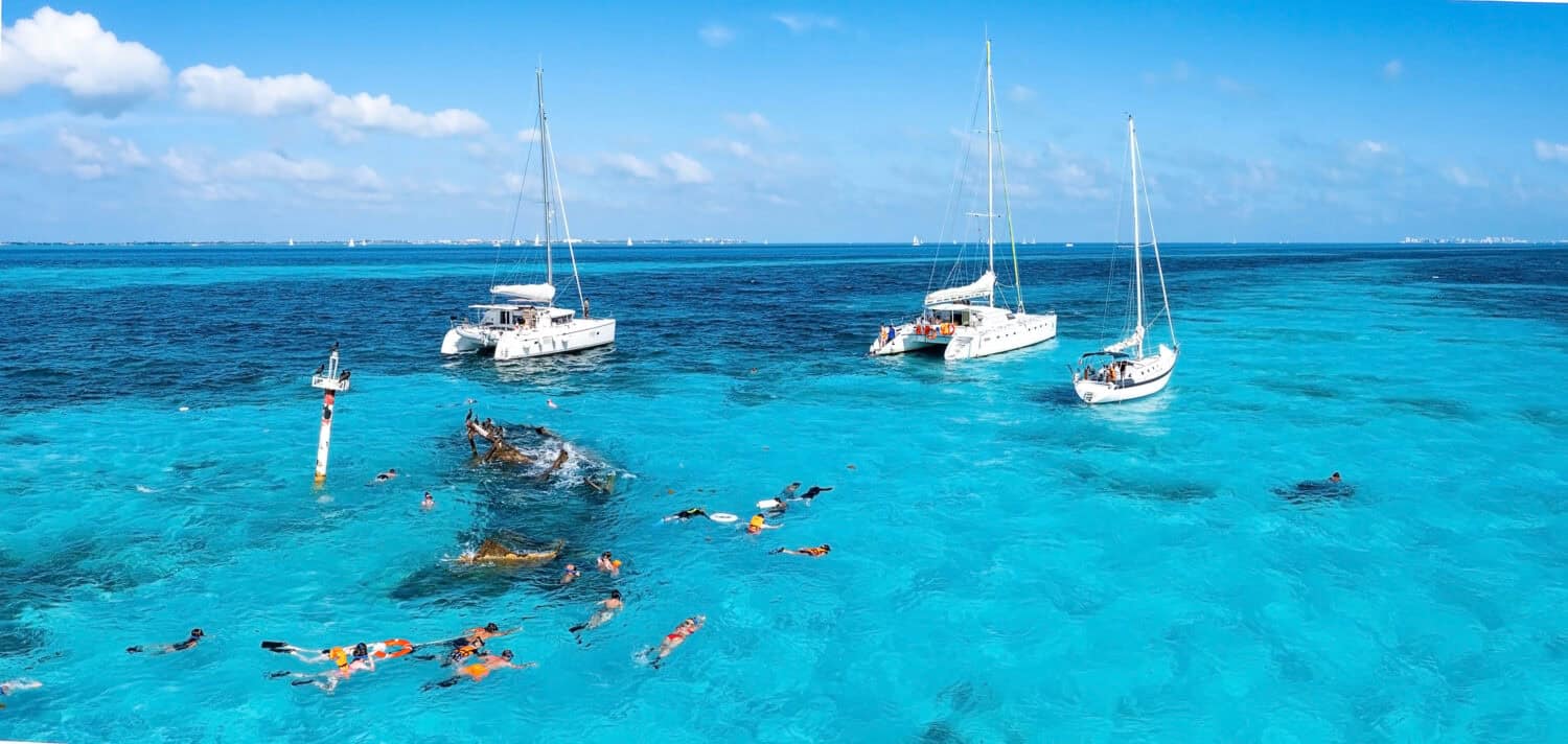 People snorkelling around the ship wreck near Cancun in the Caribbean sea. Beautiful turquoise water with people swimming with fishes, aerial view.