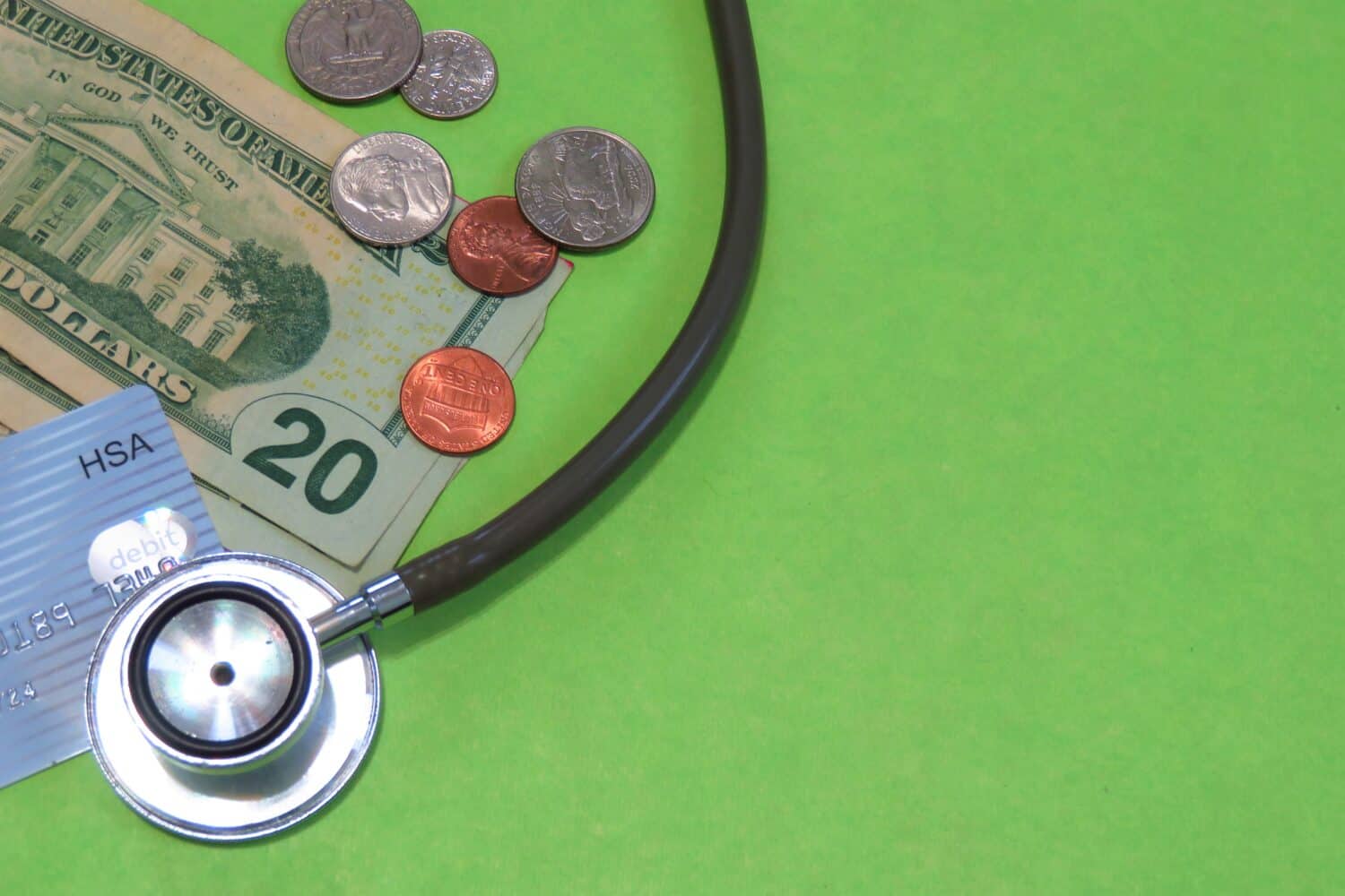 Health Savings Account portrayal: A stethoscope, HSA debit card, and US money on a green background with copy space.