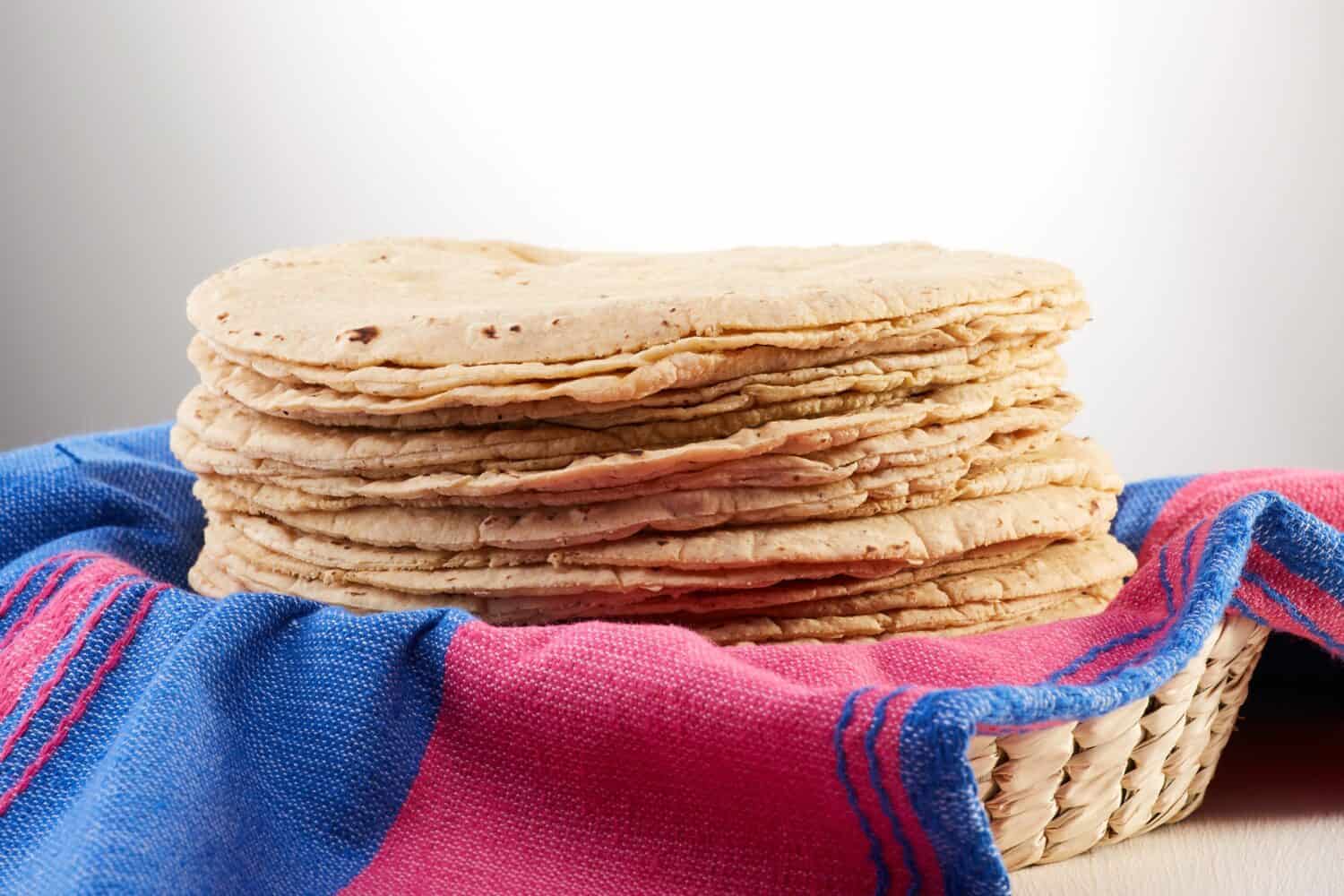 Pile of freshly made tortillas over a Mexican pink and blue cloth or napkin in a basket.