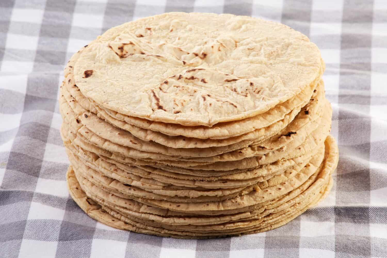 One kilo of fresh stacked tortillas on a white and grey checkered cloth.
