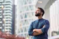 Confident rich eastern indian business man executive standing in modern big city looking and dreaming of future business success, thinking of new goals, business vision and leadership concept.