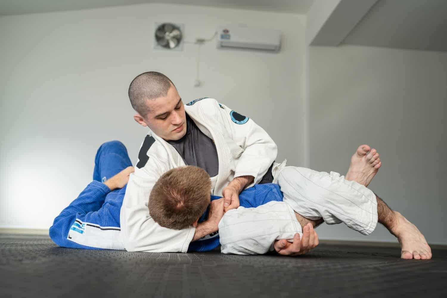 two athletes training Brazilian jiu jitsu kesa gatame side control hold BJJ in a kimono gi uniform at the academy