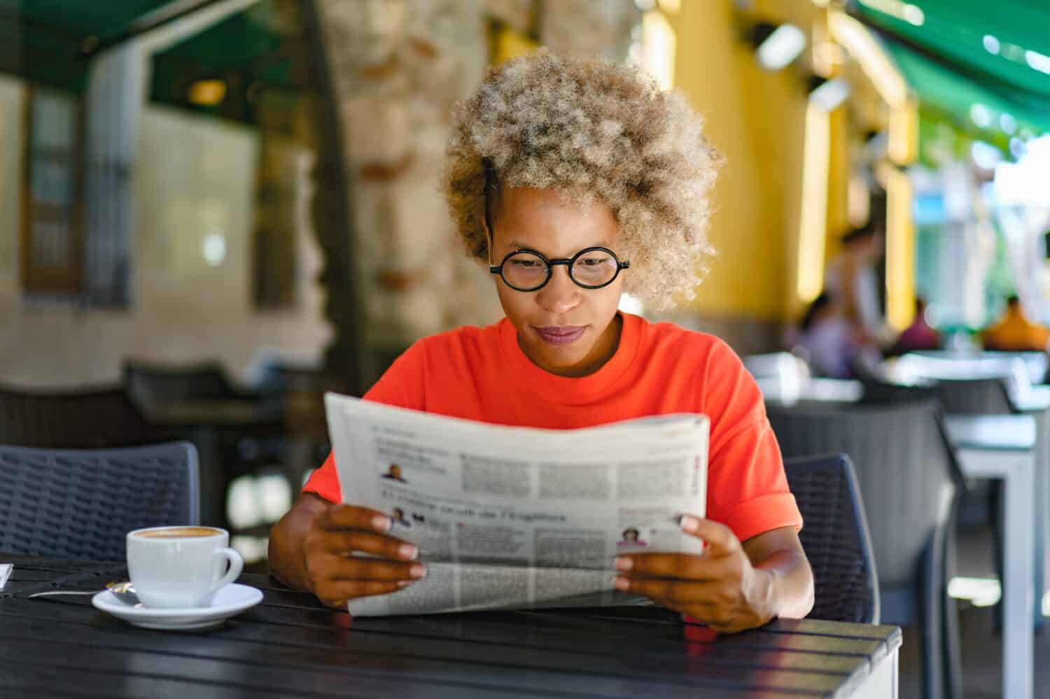 Woman drinking coffee and reading newspaper at cafe. Leisure and news concept
