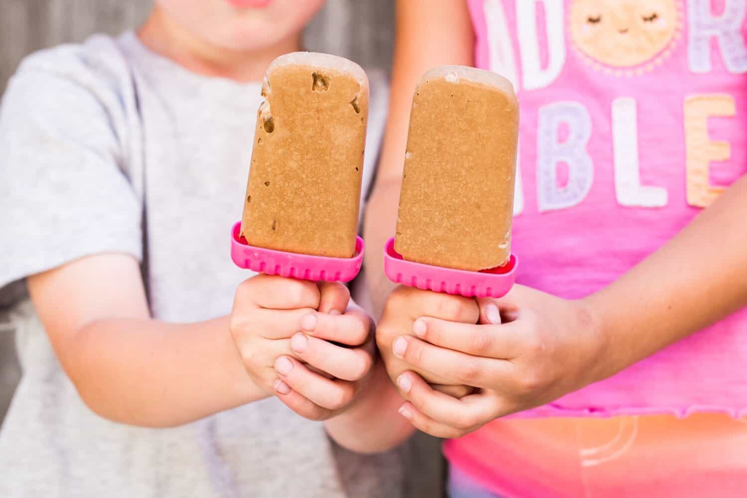 The kids holding homemade tasty frozen pudding pops on the blurred background