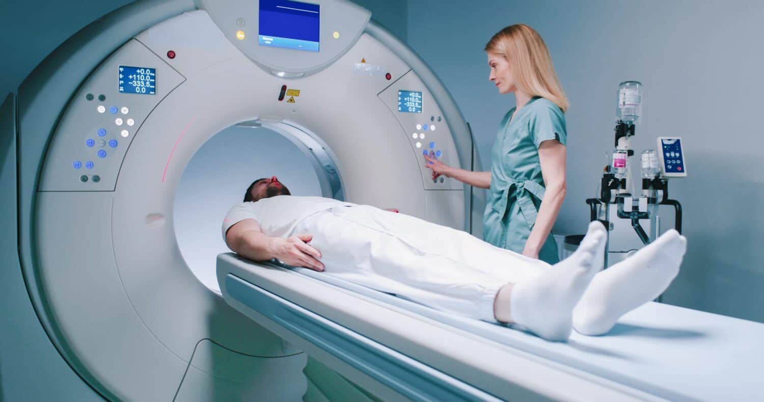 Patient is preparing for MRI examination. Man enters into MRI capsule. Female doctor calms patient and conducts magnetic resonance imaging. Medical worker is pressing buttons on MRI capsule.