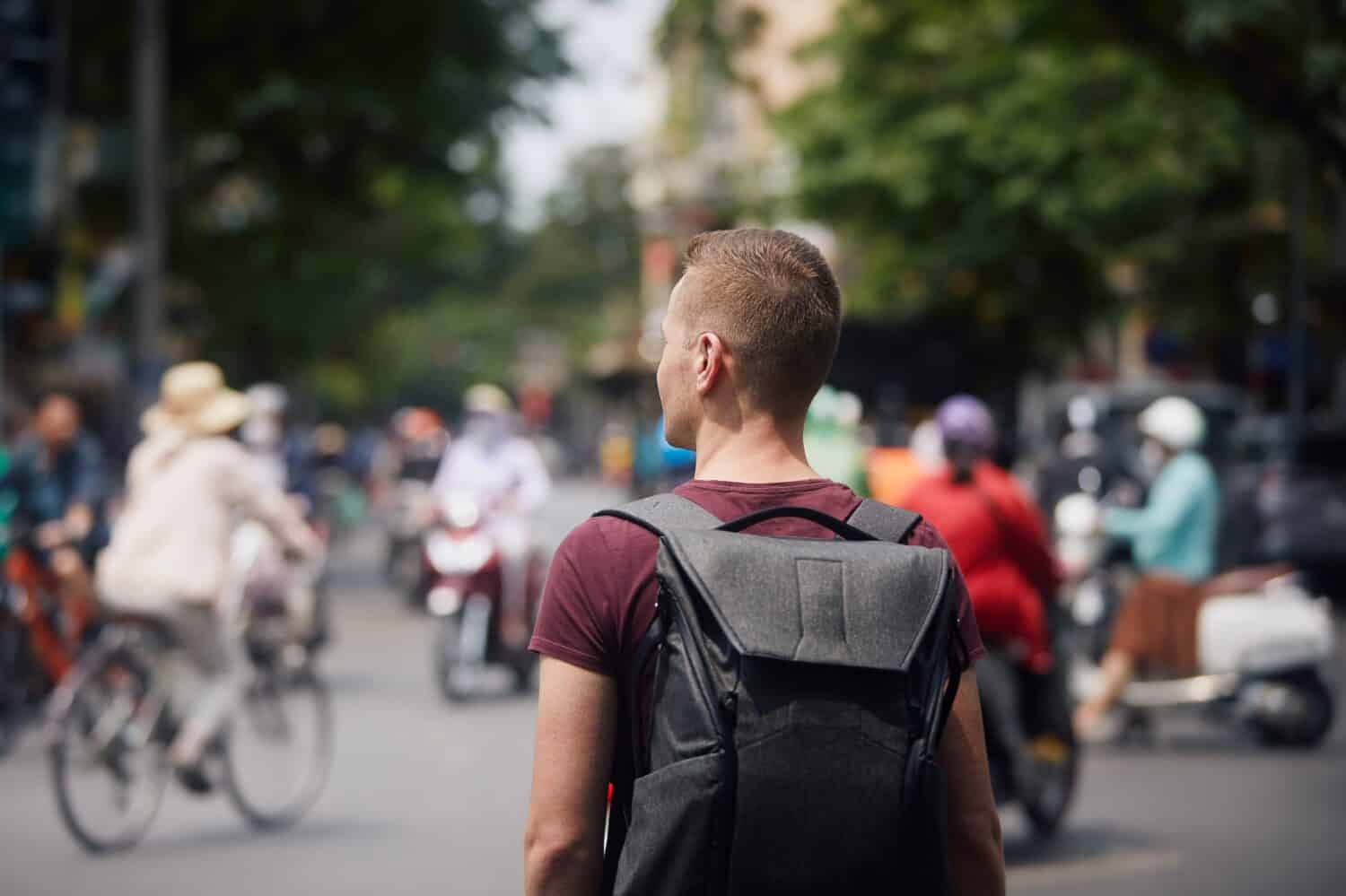Traveler with backpack discovering Vietnam. Man in the middle of a busy street full of motorbikes and bicycles in Hanoi, Vietnam.