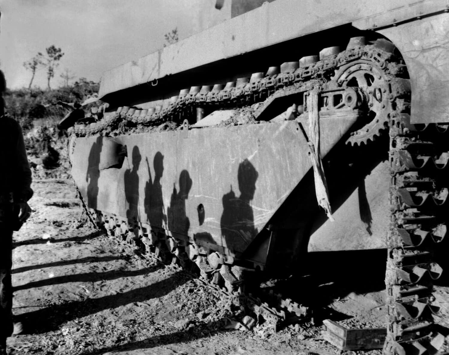 Shadows of 6th Division Marines on a battle-wrecked tank on Okinawa. The soldiers are advancing to mop up operations in the southern tip of the island. Late May to early June 1945.