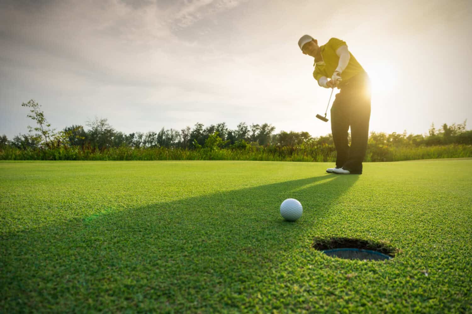 Golfer putting golf ball on the green golf, lens flare on sun set evening time.