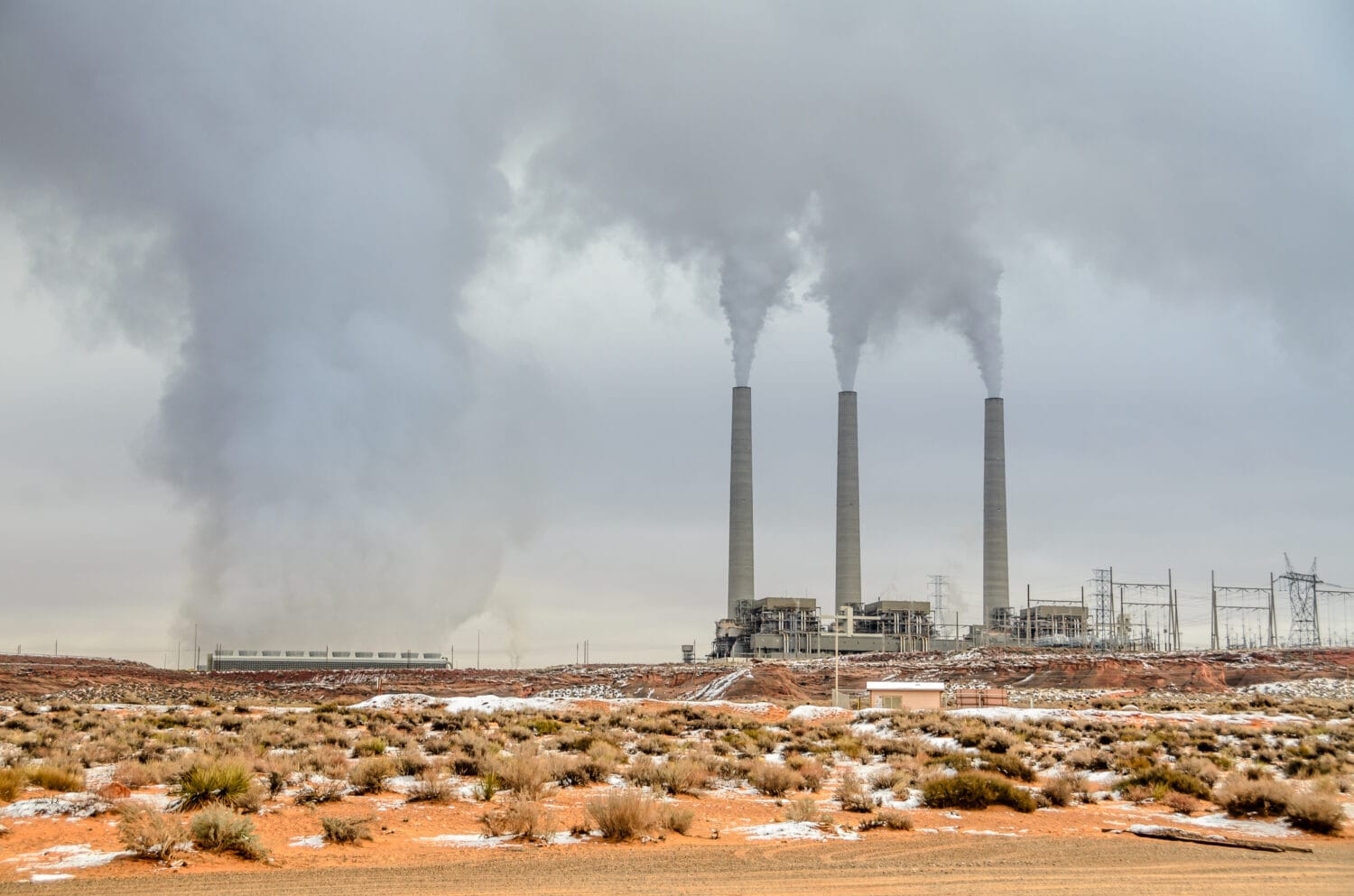 View of smoking smoke stacks of a generating station at the Navajo reservation, Arizona, USA. Desert landscape violated by an air polluting power plant, smog and gloomy sky. Polluting energy source.