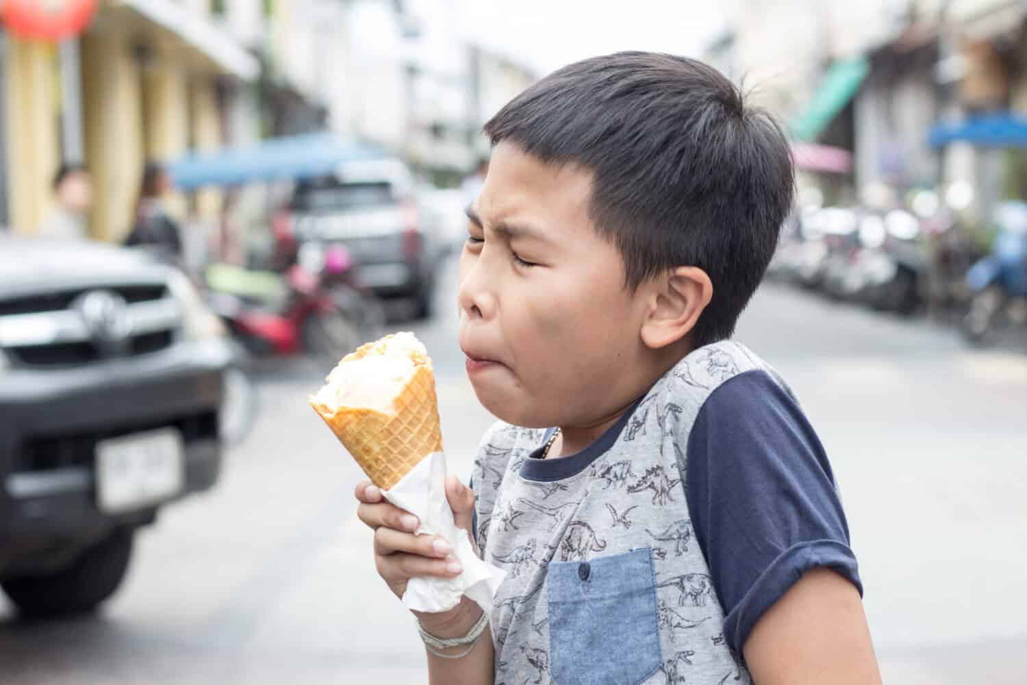 An Asian boy experiences brain freeze due to ice cream cone.