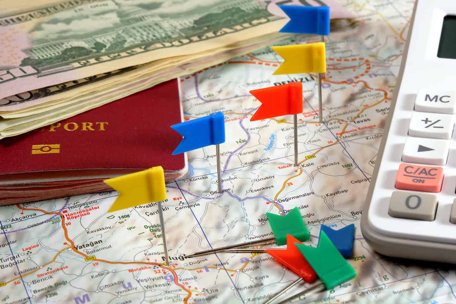 pin flags marking travel itinerary points on map and passport, dollar banknotes and calculator