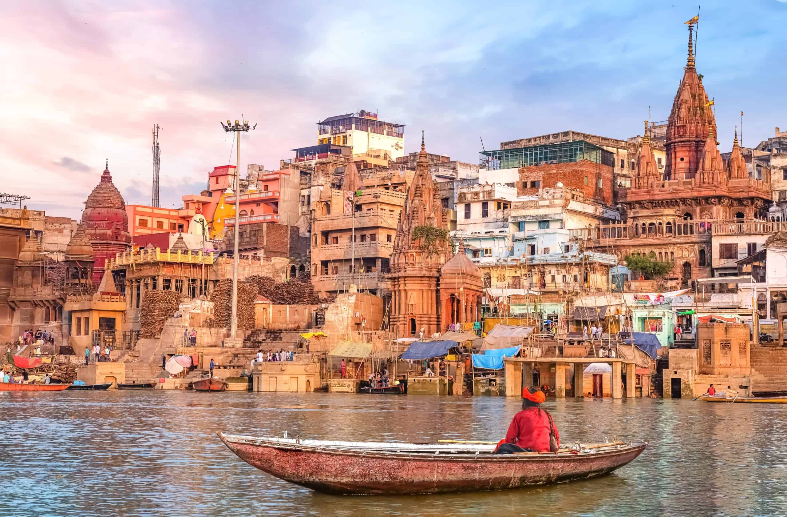 India | Hindu sadhu sitting on a boat overlooking Varanasi city architecture at sunset