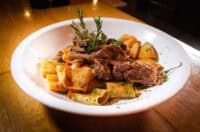 close up of traditional italian dish, paccheri pasta with slow cooked pork short ribs, eating in a fine dining italian restaurant, cool ambience, sharing with loved ones