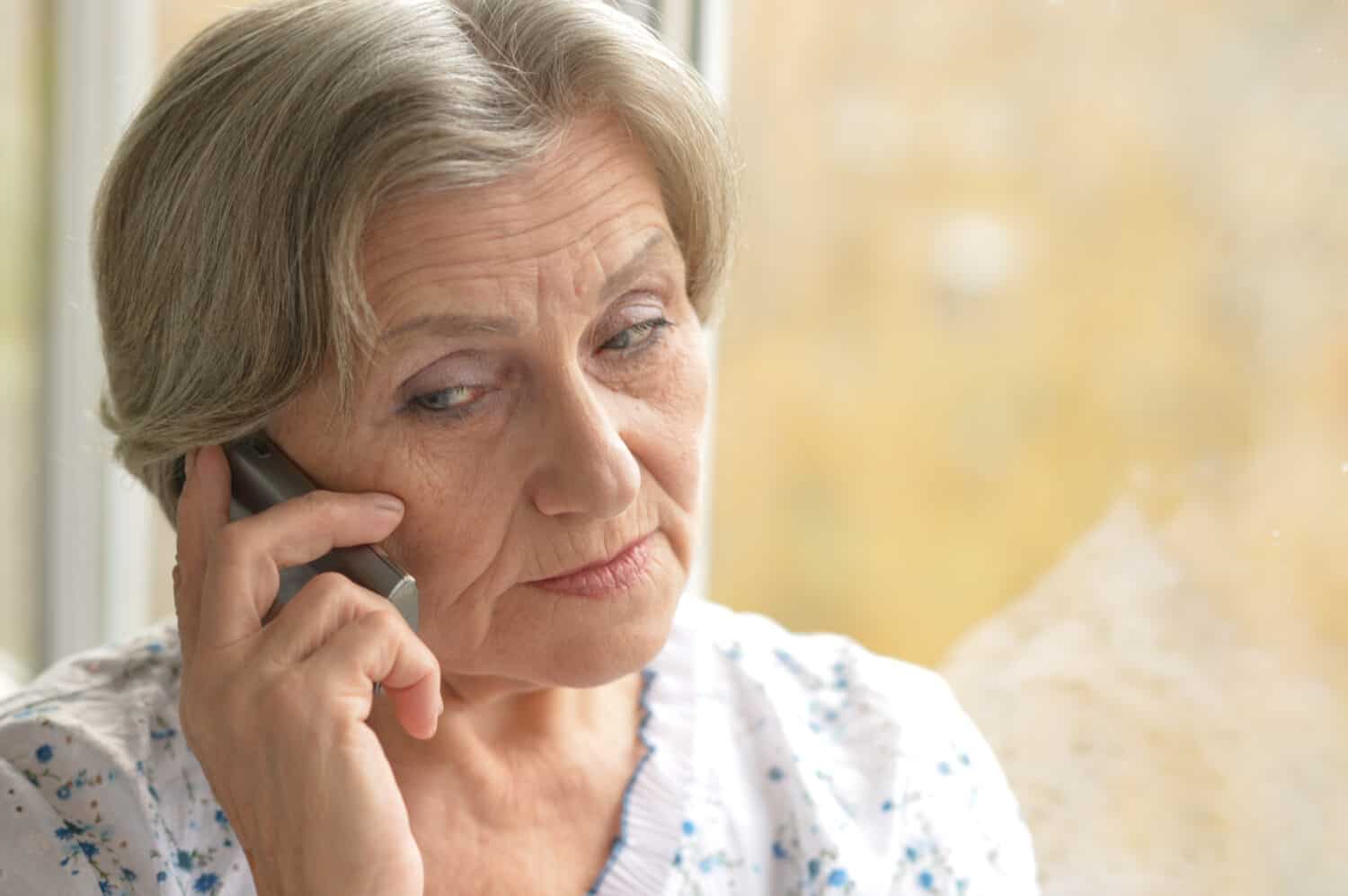 Miling senior woman calling on phone at home