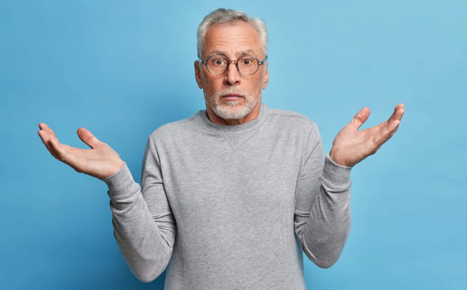 Questioned puzzled grey haired man spreads hands in clueless gesture shrugs shoulders has to make choice dressed in casual clothes cannot understand whats wrong looks with perplexed expression
