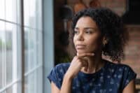 Close up thoughtful African American woman looking out window to aside, touching chin, dreamy young female lost in thoughts, planning, visualizing future, businesswoman thinking, making decision