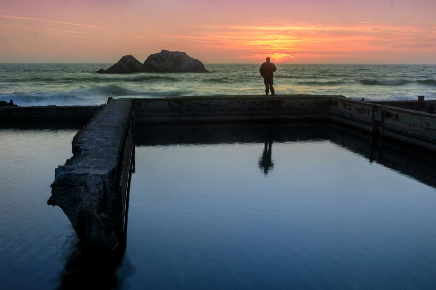 A man standing on ruins of Sutro Baths and watching the sunset. San Francisco, California, USA.