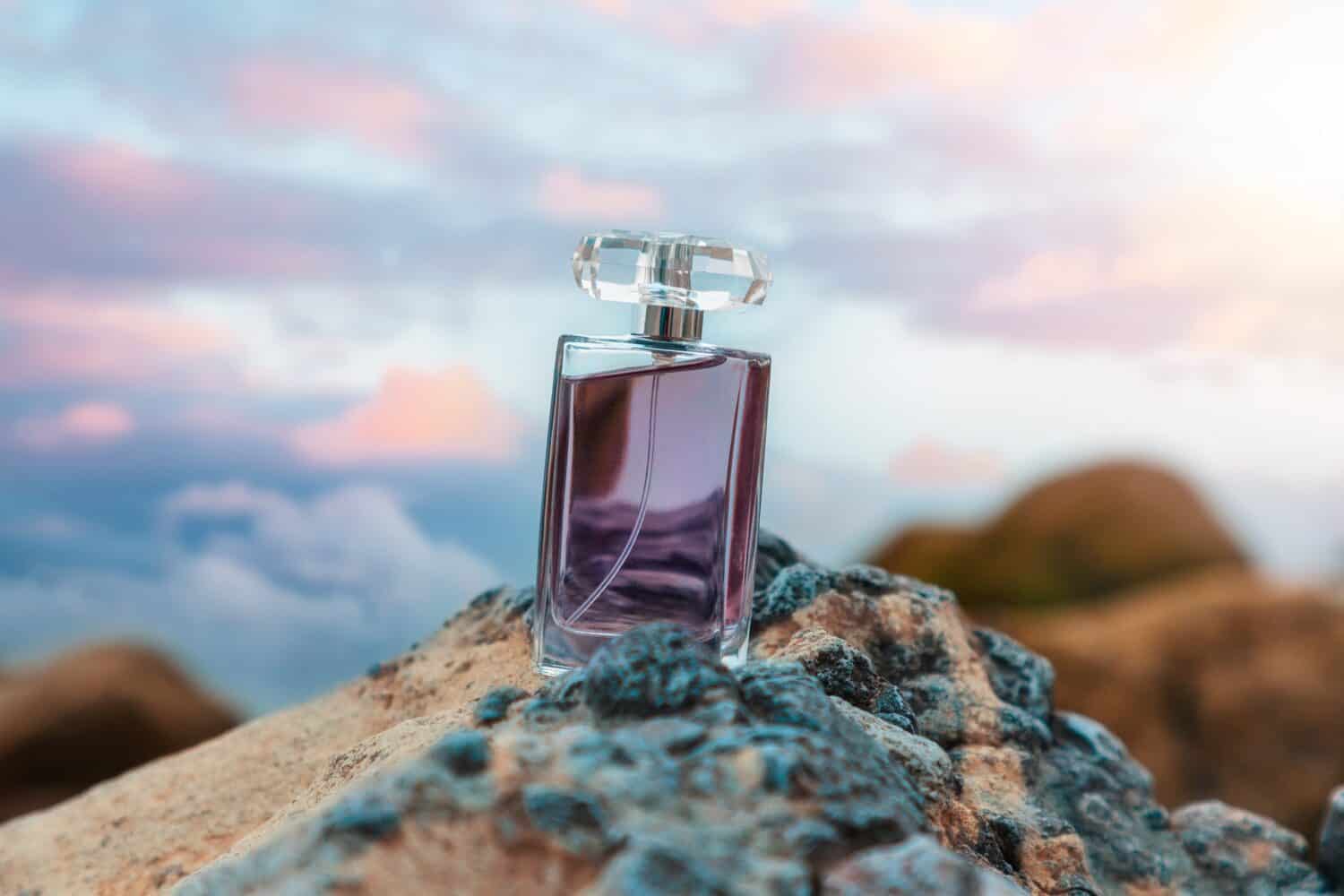 Transparent bottle with purple perfume on rock. Copy space. Concept of luxe perfumery and cosmetics