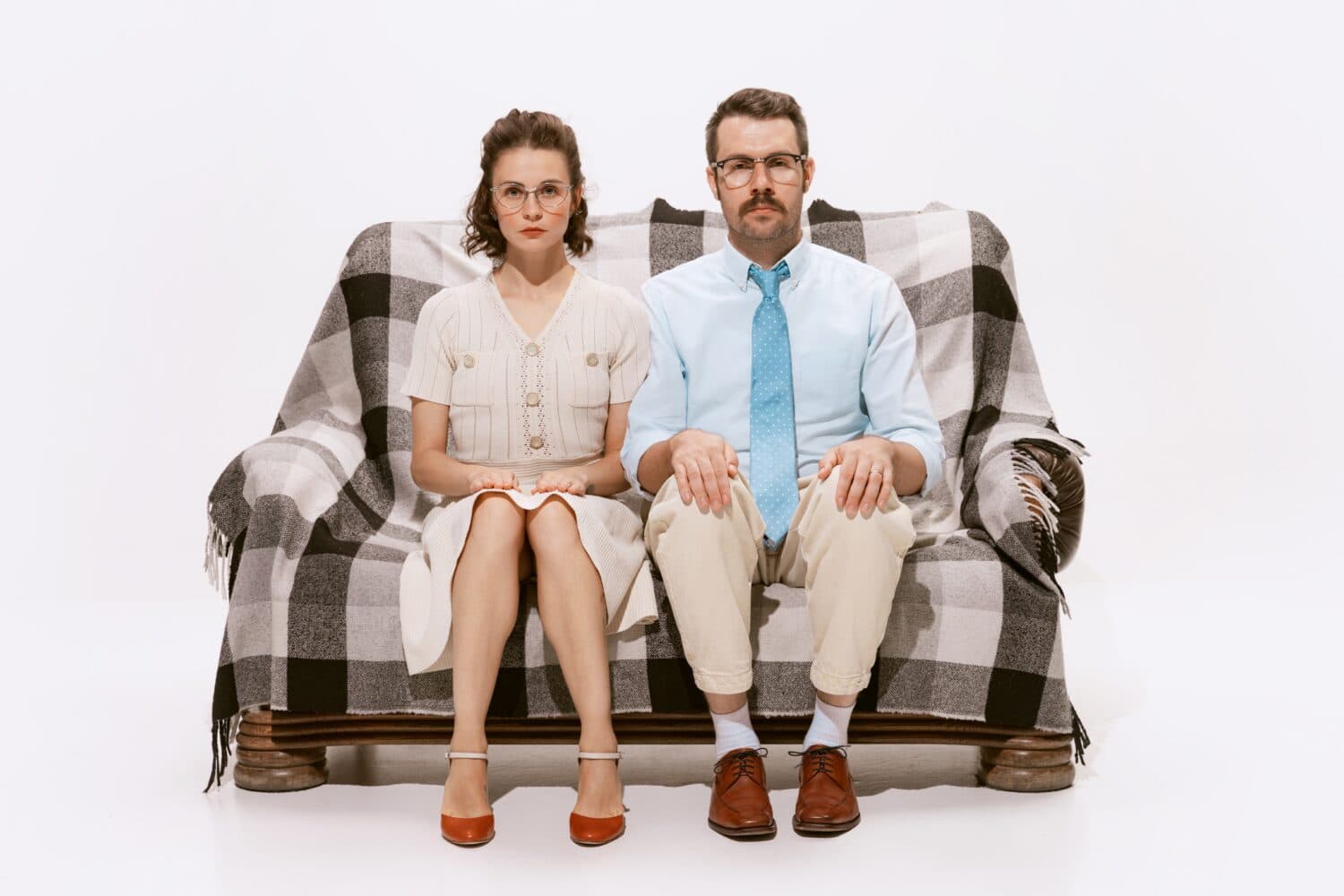 Portrait of serious man and woman sitting on sofa and looking at camera isolated over white background. Concept of love, relationship, retro style, creativity, family. Copy space for ad