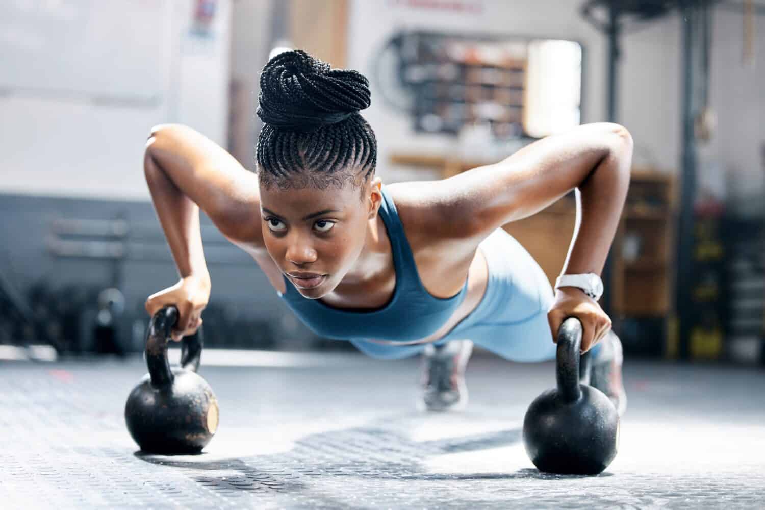 Fitness, push up or black woman with kettlebell for training, body workout or exercise at health club. Motivation, mindset or African girl sports athlete exercising with focus or resilience at gym