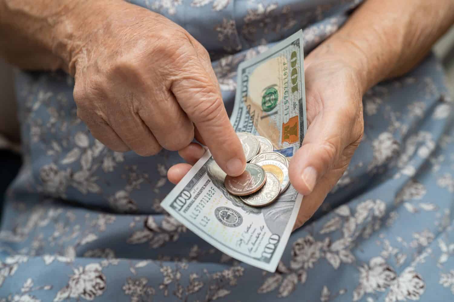 Asian senior woman holding and counting US dollar banknotes with coins money in purse. Poverty, saving problem in retirement.