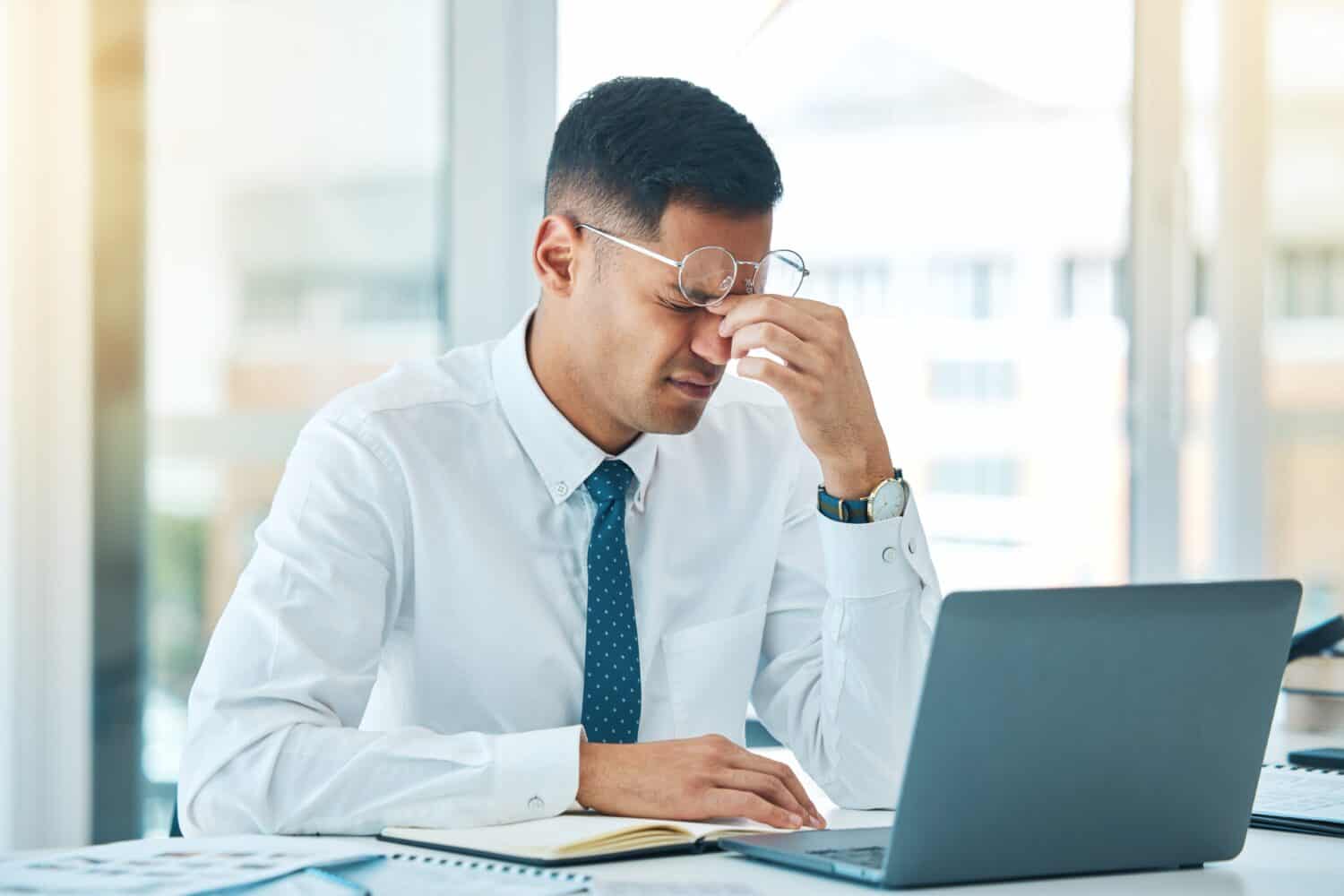 Business man, headache and stress on laptop for financial mistake, accounting error or results and pain. Professional person with glasses, tired and fatigue on computer for research and job report