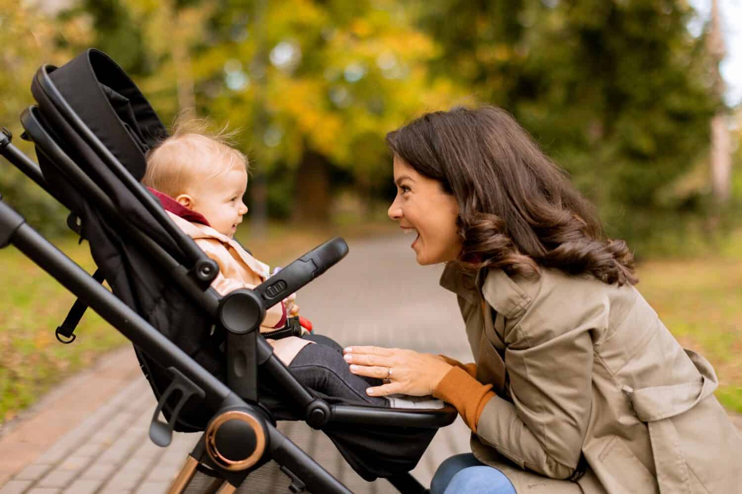 Young woman with a cute baby girl in baby stroller at the autumn park