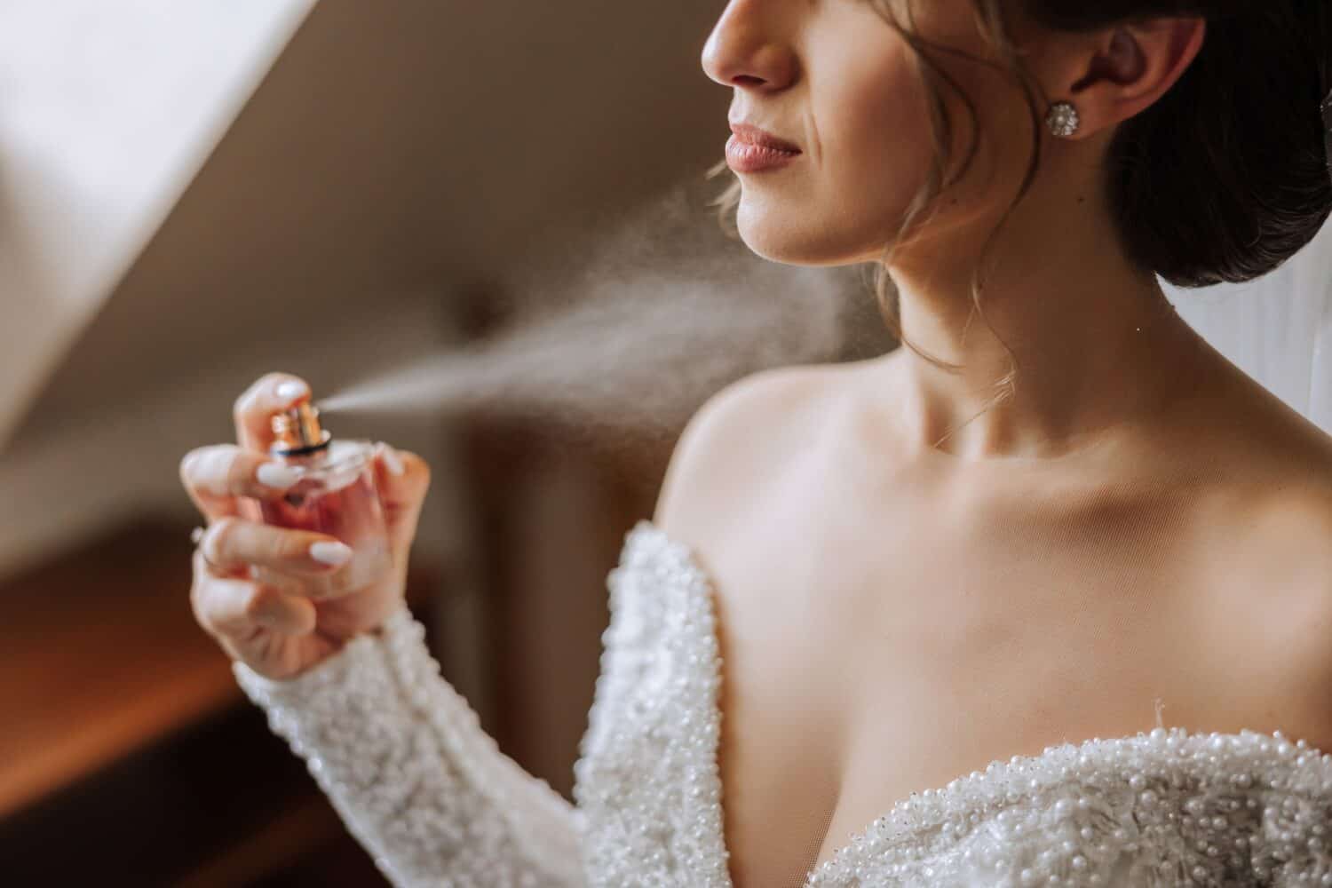 The brunette bride, holds perfume in her hands, wants to apply it on herself. Voluminous veil. Beautiful hands. Open bust