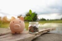 Saving money by hand puting coins in jug glass on nature background