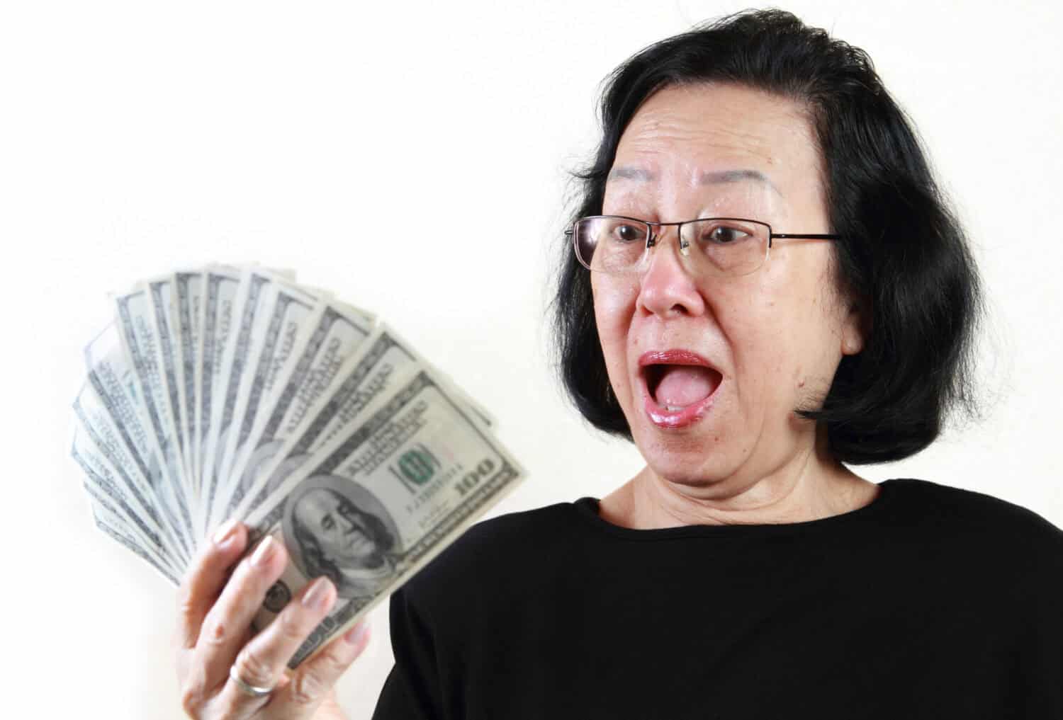 Asian lady holding a bunch of $100 bills with surprised facial expression