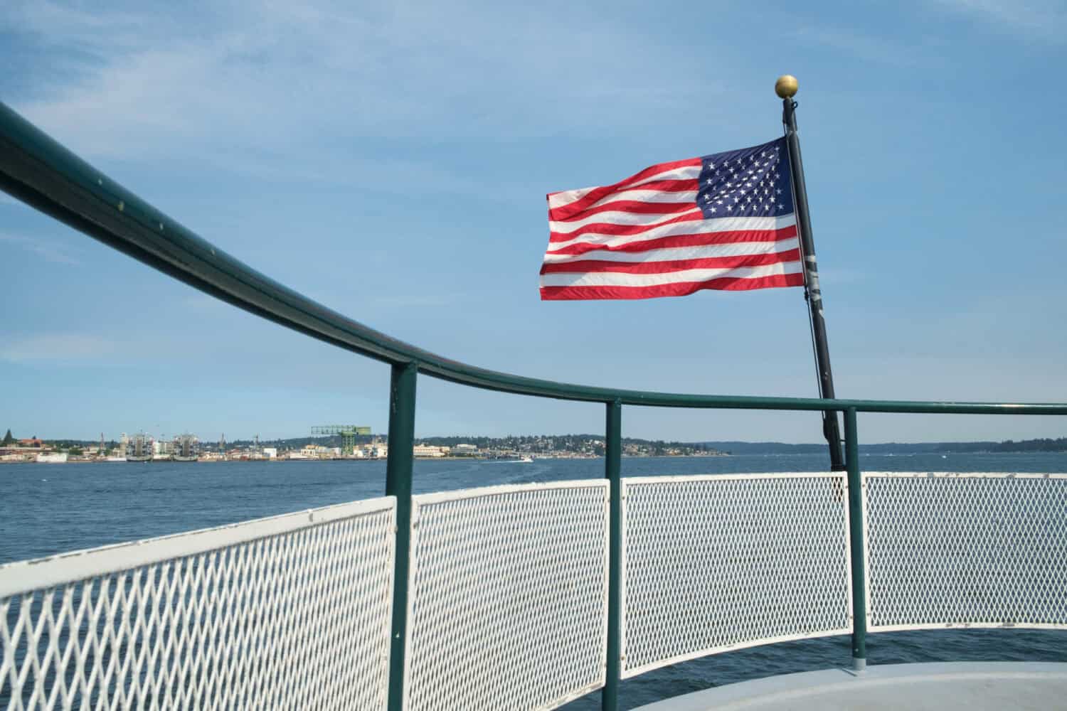 American flag blowing in breeze at stern of passenger ferry crossing Sinclair Inlet from Bremerton, Washington to Port Orchard, Washington with Puget Sound Naval Shipyard in background