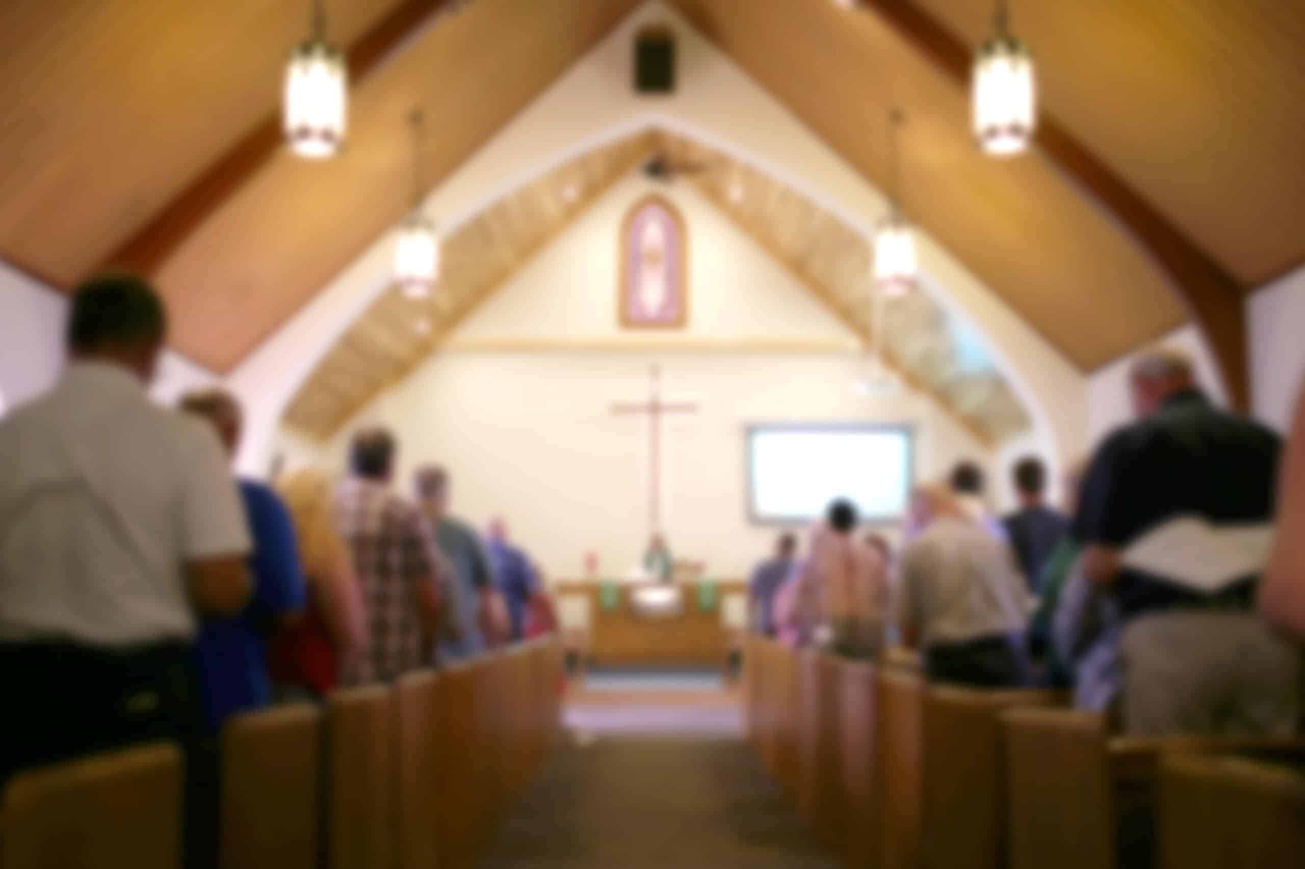 church service | Blurred Photo of the Iterior of a Church Sanctuary with Congregation, Pastor, and a Large Cross Visible