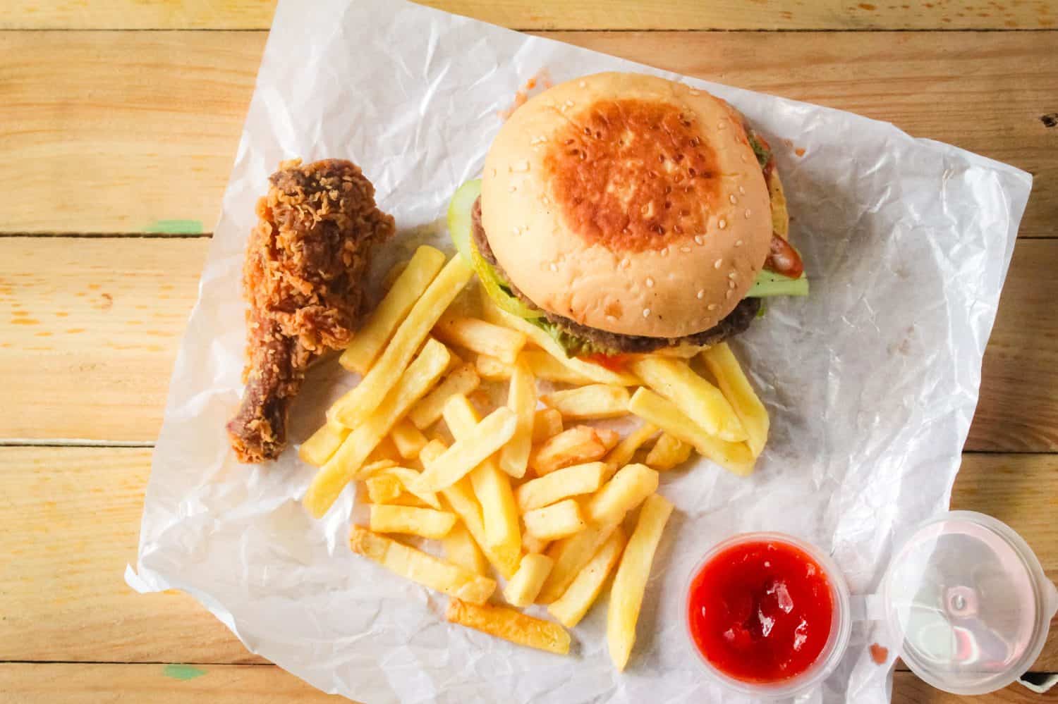several types of fast food such as hamburgers, french fries, fried chicken and tomato sauce on a wooden table.