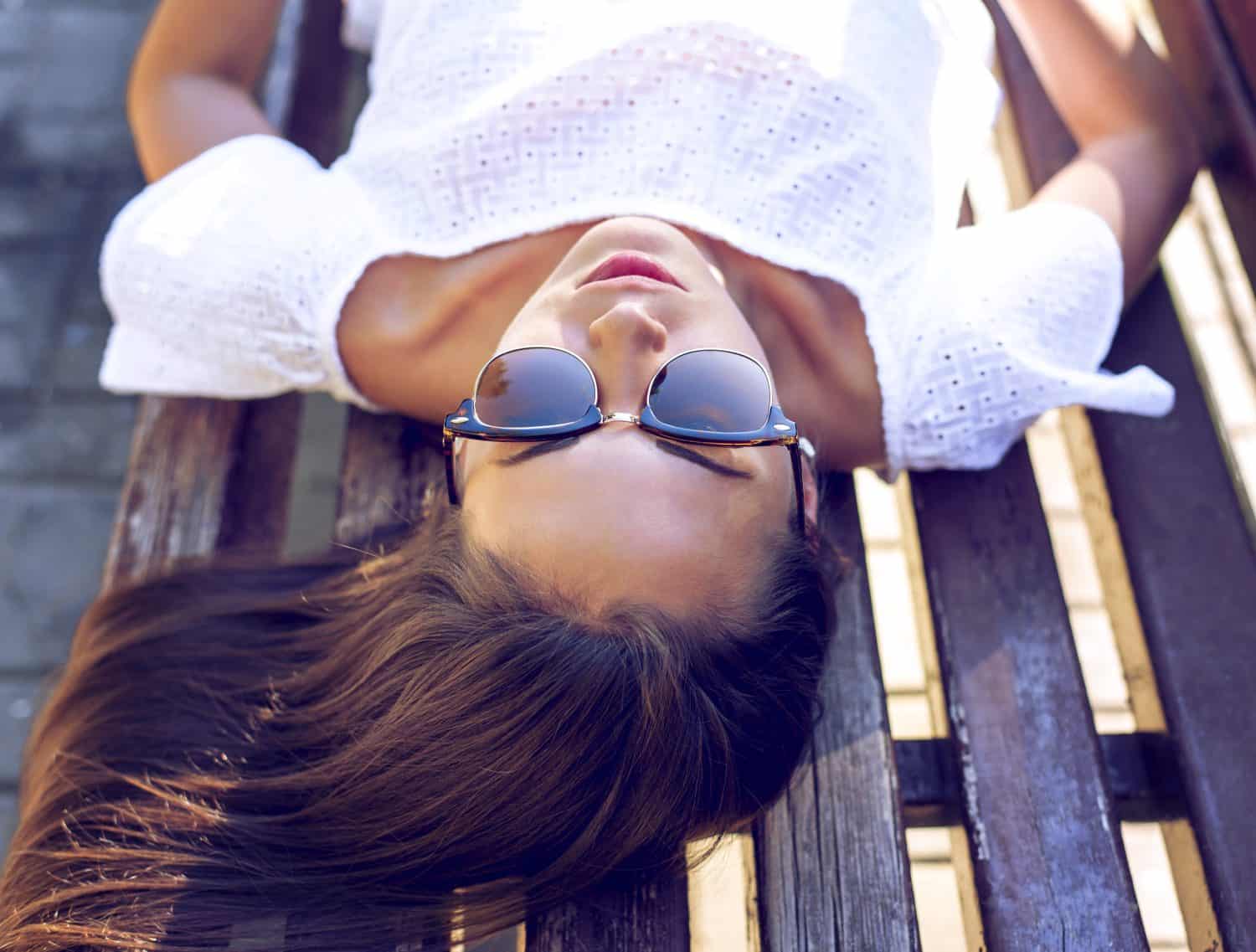 Beautiful brunette student girl lying on a park bench relaxing in the fresh air. Fashion style glamorous woman, summer day in the city during the day on a bench sleeping, sunbathing.